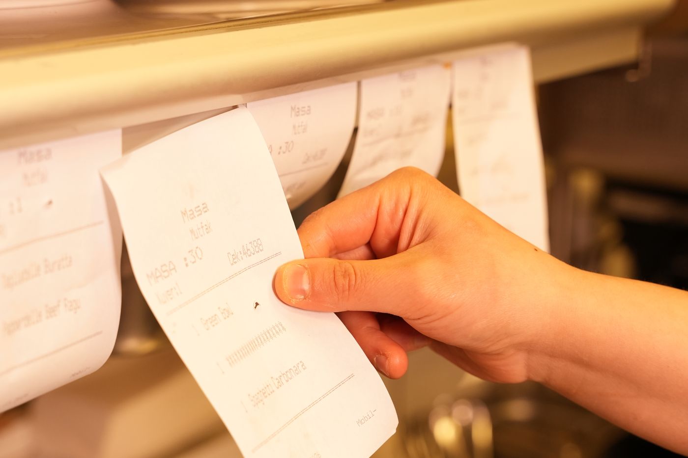 A hand pulling a ticket off the rail in a restaurant kitchen, the sales side of the sales per labor hour formula